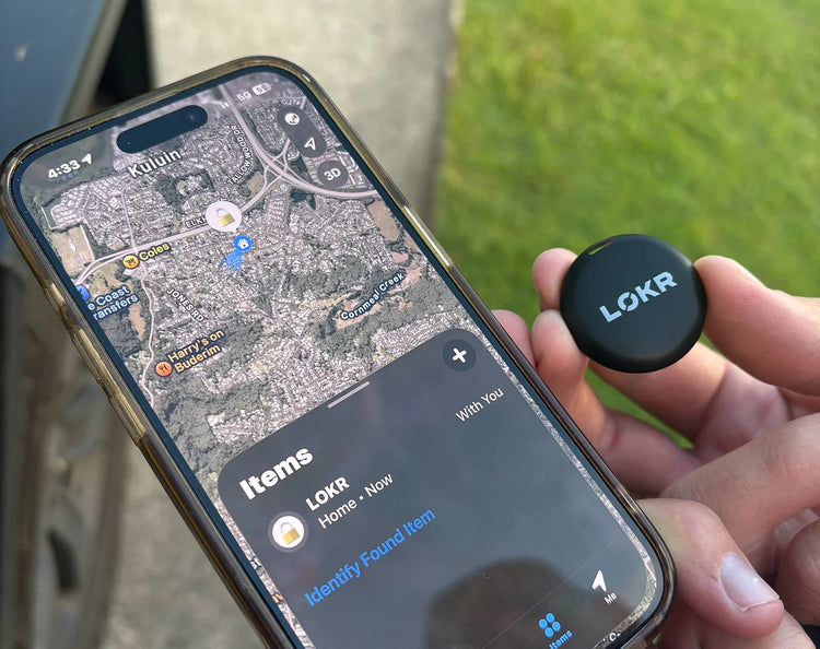 a person holding a LOKR tracker tag next to a smartphone. The phone screen displays the Apple Find My app tracking map showing the tag's current location