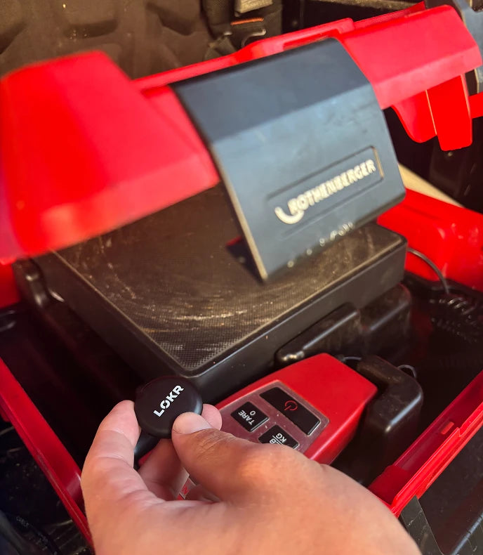 a person's hand holding LOKR tracking tag inside a red equipment box next to a tool scale component