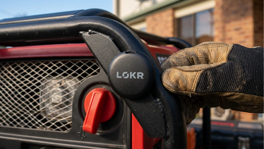 A gloved hand attaching a LOKR tracking tag to the black metal frame of a red generator