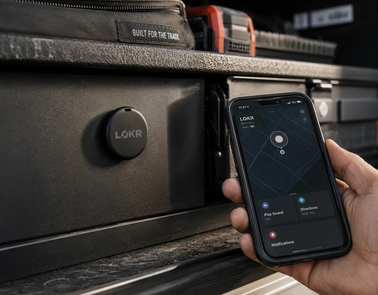 LOKR tracking tag mounted on a heavy metal storage drawer next to a hand holding a smartphone with a location map app open