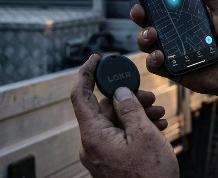 A close-up view of a person holding a LOKR tracking tag on it next to a smartphone