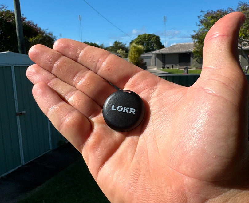 LOKR tracking tag sits in the palm of an open hand outdoors