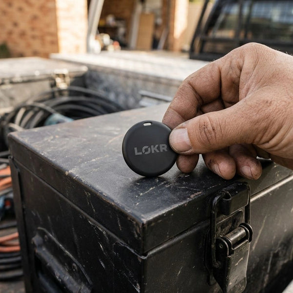 a LOKR tracking tag sitting on top of a weathered, black metal equipment box being held by a hand