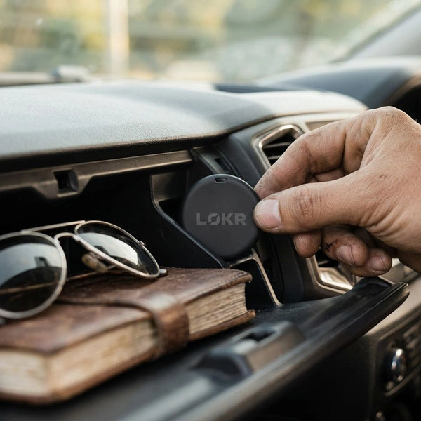 a person placing a LOKR tracking tag onto a car's dashboard vent next to a pair of sunglasses and a notebook